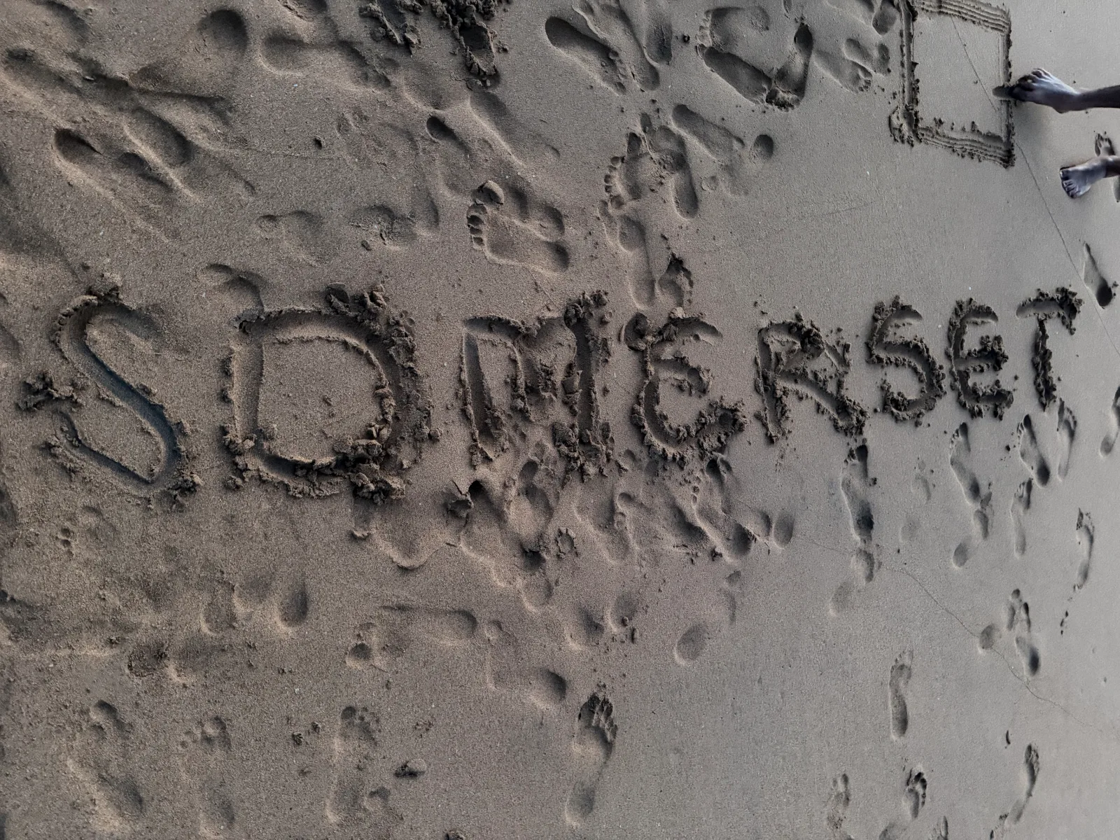 The word "Somerset" written in the sand on the beach, among footprints